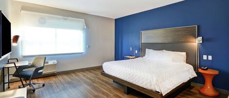 Une chambre d’hôtel moderne, dotée d’un grand lit, d’un bureau avec une chaise, d’une petite table et d’une fenêtre avec des stores.