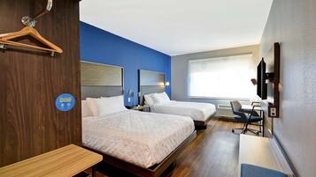 A hotel room with two beds, a desk, a chair, a TV, and a window.