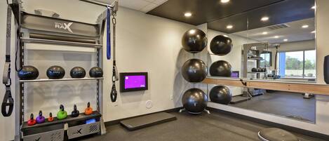 A gym with exercise equipment, a mirror, and a digital screen.
