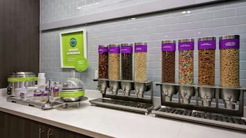 Una barra de desayuno con dispensadores de yogur y avena, un cartel que indica yogur y avena, y varios dispensadores de cereales.