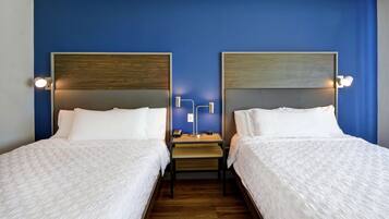 A hotel room with two beds, each with a wooden headboard and white bedding. There is a small table between the beds with a lamp and a phone.