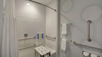 Un baño moderno con ducha, barras de apoyo, un pequeño banco y dispensadores de gel antibacterial.