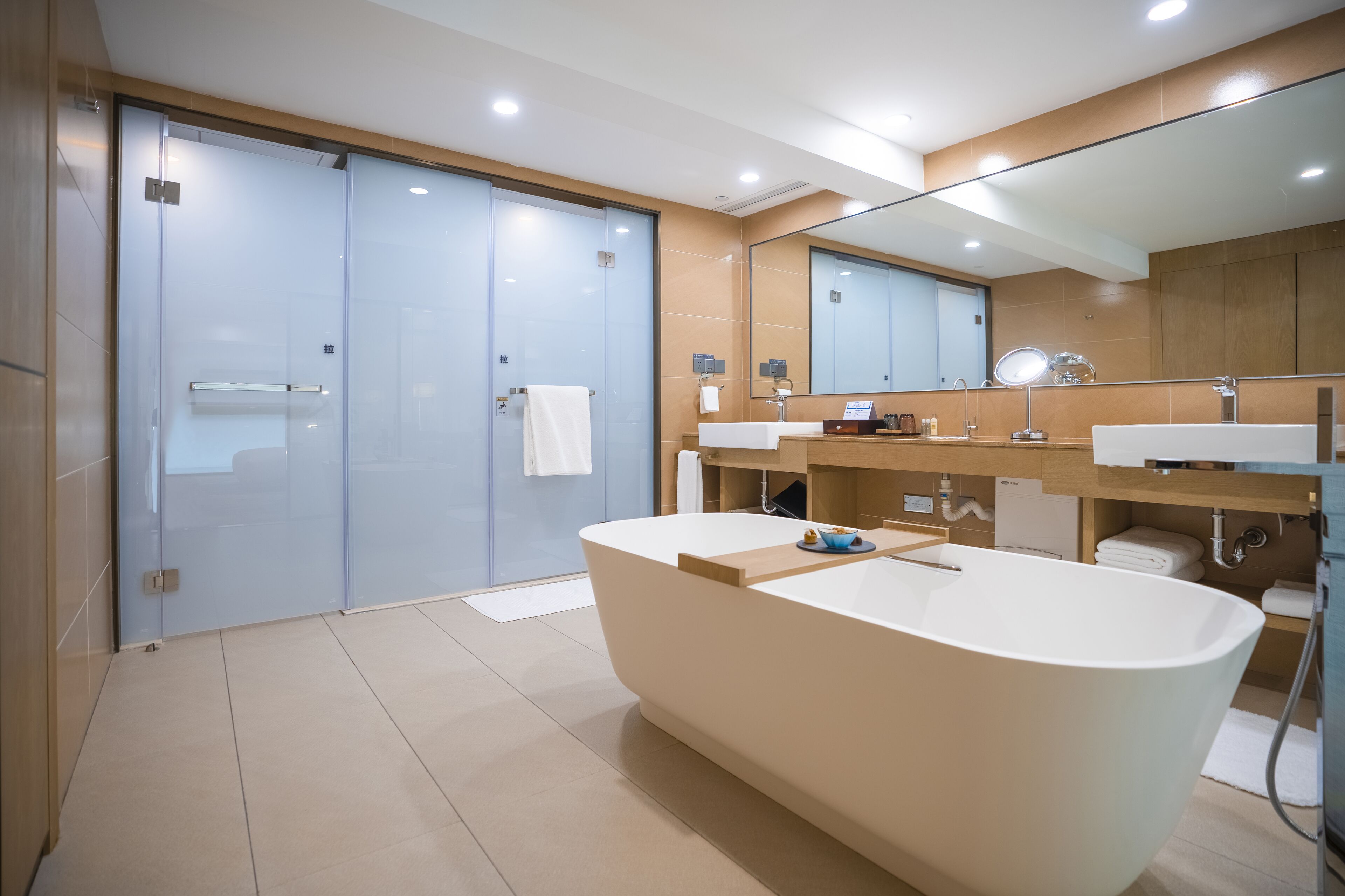 A modern bathroom with a freestanding bathtub, two sinks, a large mirror, and a glass shower enclosure.