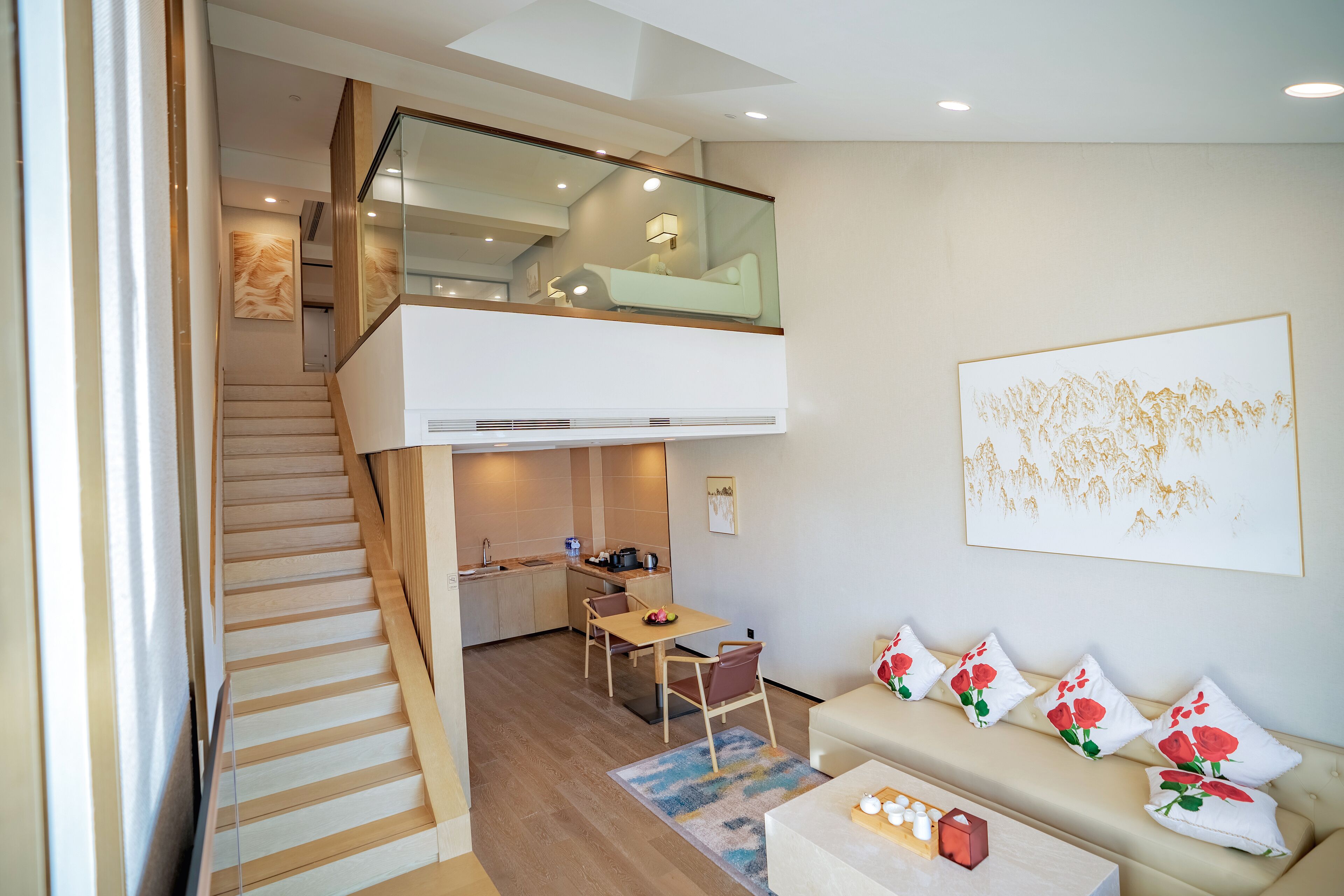 A modern apartment with a staircase leading to a loft bedroom, a dining area, and a living room with a sofa and decorative pillows.