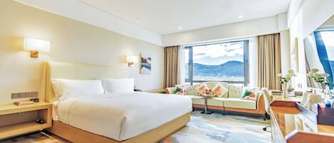 Habitación de hotel con una cama grande, un sofá, un escritorio y vistas a las montañas desde la ventana.