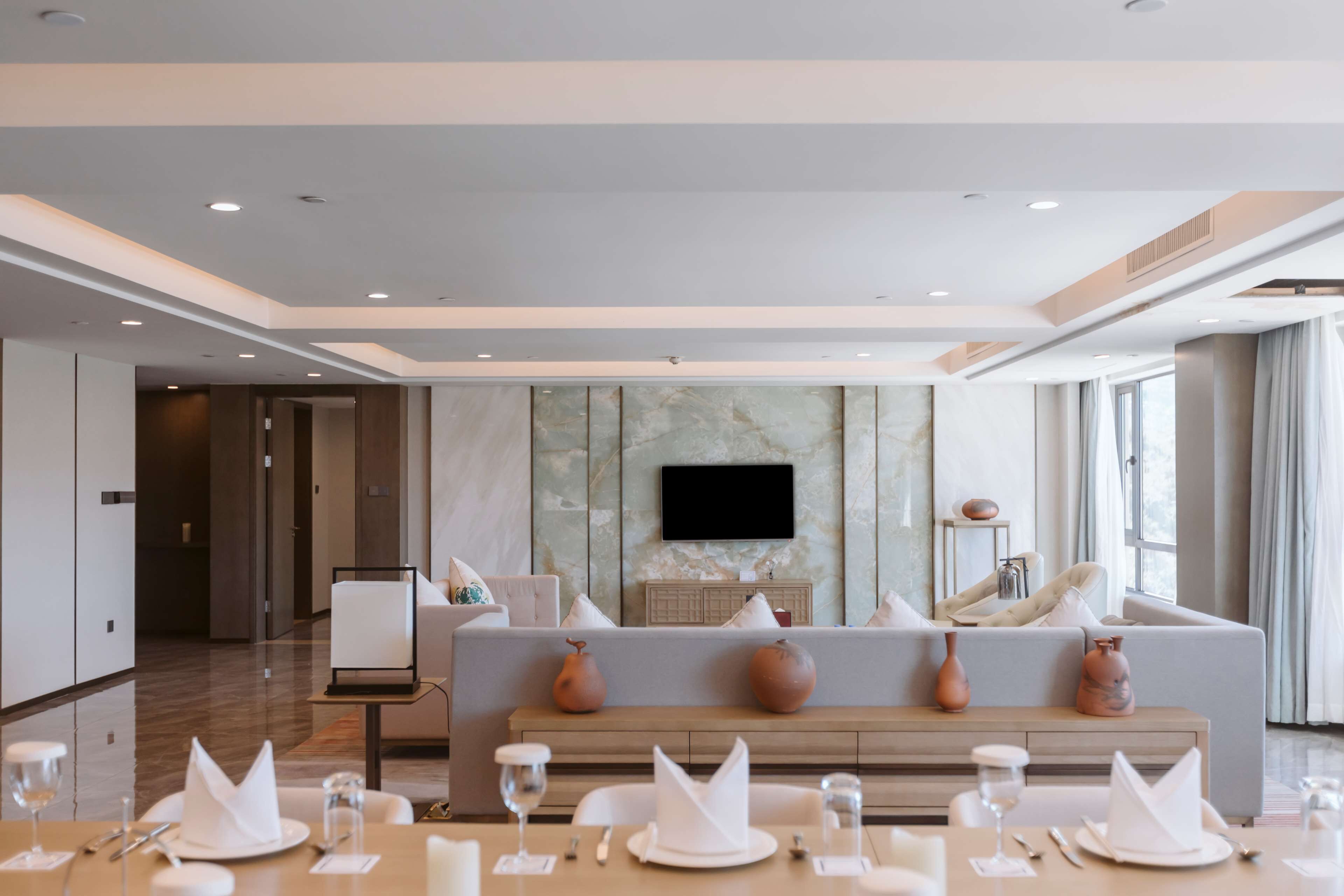 Une chambre d’hôtel moderne, dotée d’un canapé, d’un téléviseur à écran plat fixé au mur et d’un coin repas avec des tables dressées pour le repas.
