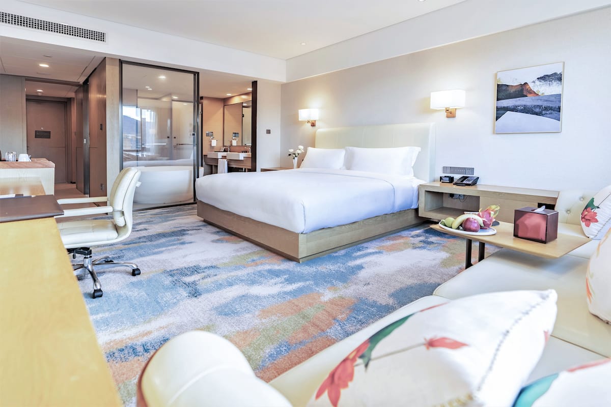 A hotel room with a bed, bedside table, chair, desk, and a carpeted floor.