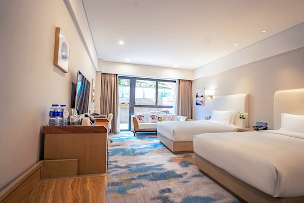 Habitación de hotel con dos camas, un escritorio, un televisor y un amplio ventanal con cortinas.