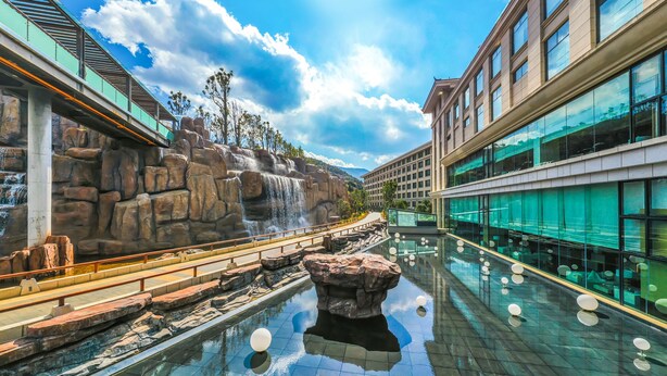 A modern hotel with a pool area featuring a waterfall and rock formations. - Hilton Lijiang (Lijiang)