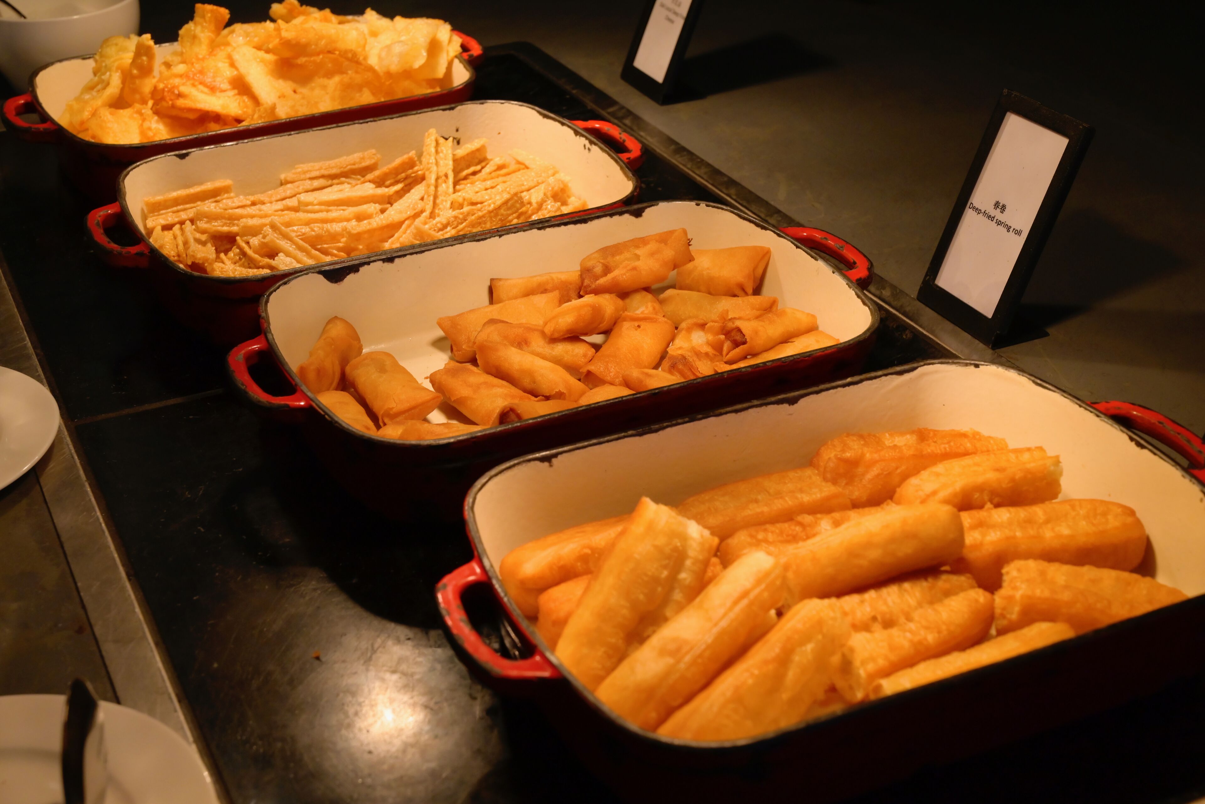 Ein Buffet mit verschiedenen Speisen, darunter Pasta, Pommes und Frühlingsrollen.