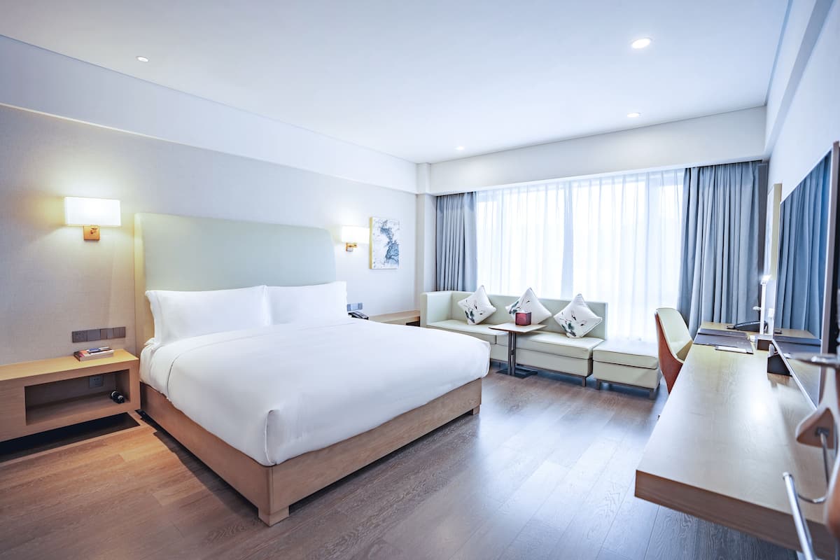 A modern hotel room with a large bed, a desk, and a sofa.