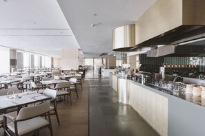 A modern restaurant with a long dining area, a central bar, and a kitchen visible in the background. - Hilton Lijiang (Lijiang)