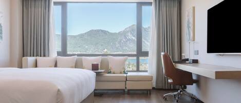 Ett modernt hotellrum med en stor säng, ett skrivbord och utsikt över bergen genom ett stort fönster.