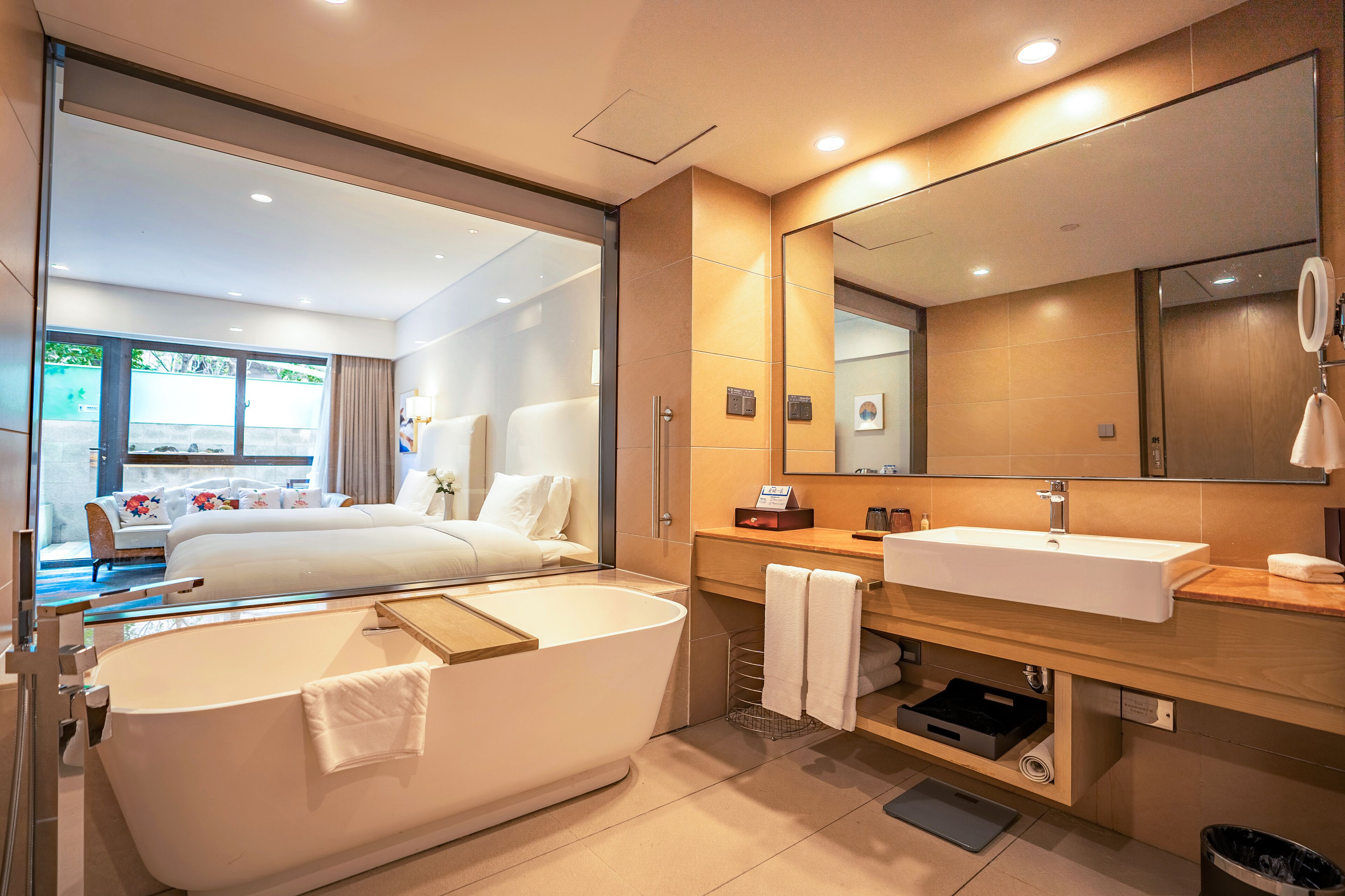 Una habitación de hotel moderna con una cama grande, una bañera, un tocador con lavabo y un espejo amplio.