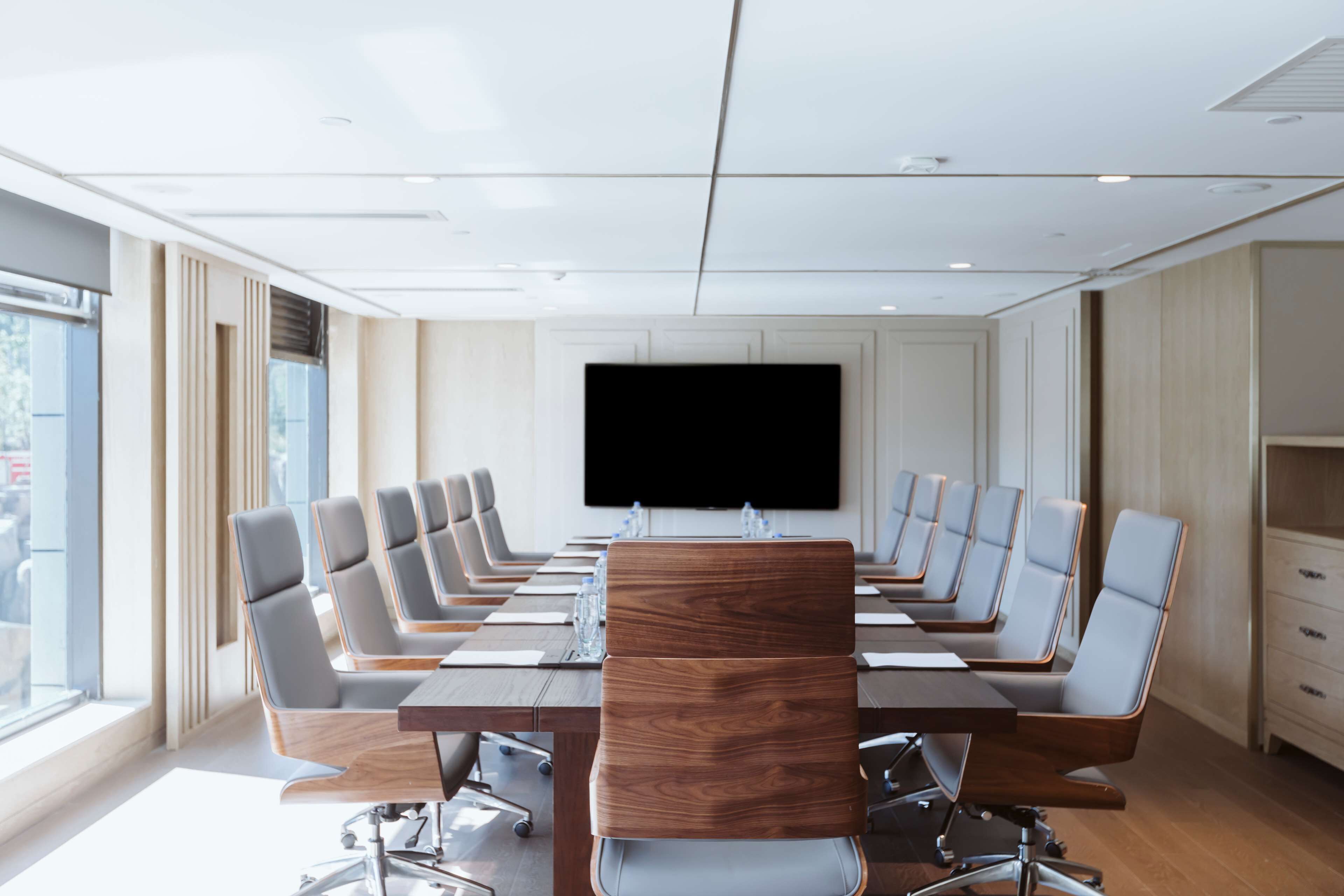 A conference room with a long table, multiple chairs, a large screen, and a window.