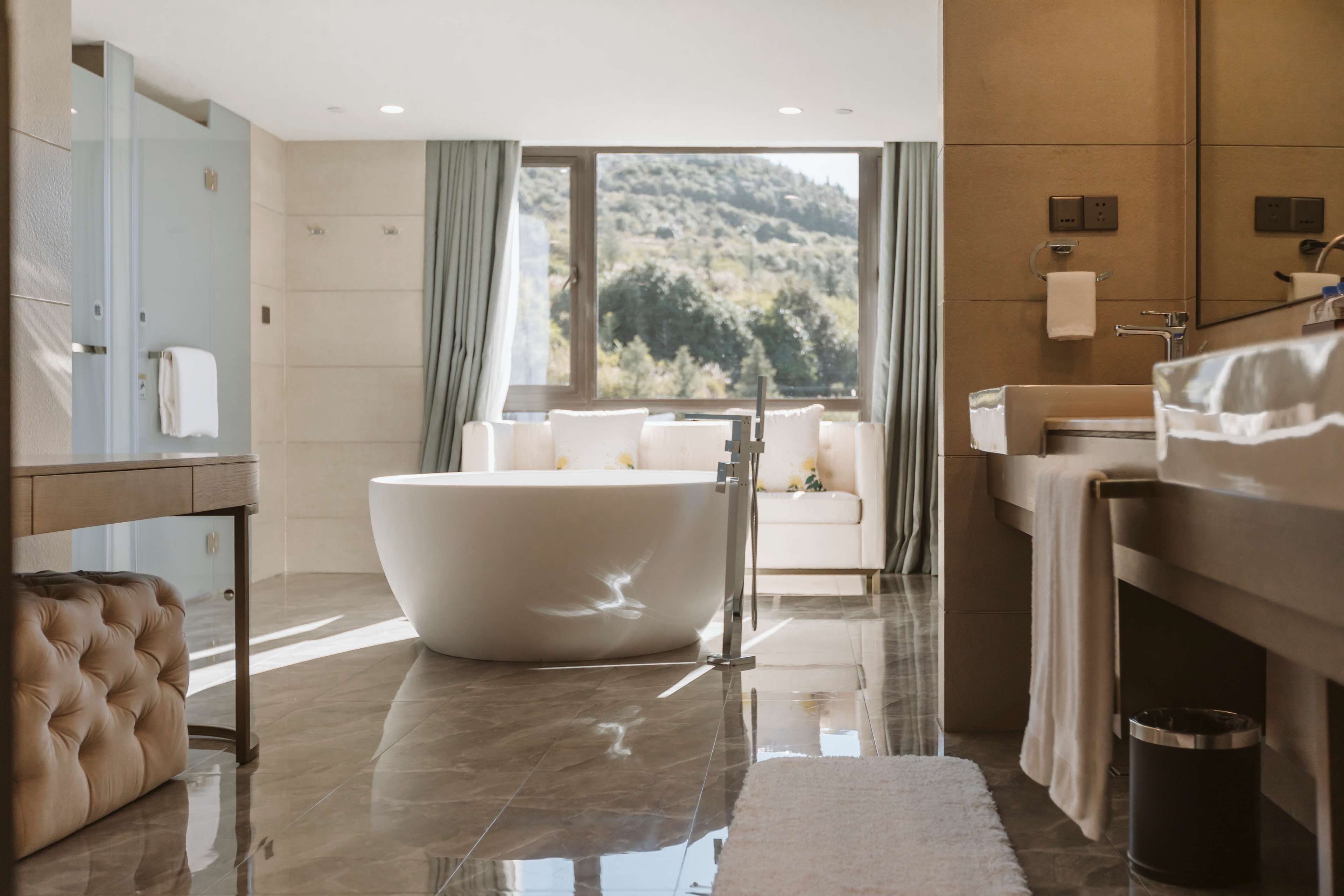 A modern bathroom with a freestanding bathtub, a vanity with a mirror, and a view of a mountainous landscape through large windows.