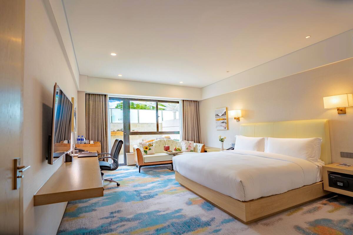 A hotel room with a large bed, a desk, a chair, a sofa, and a window with curtains.