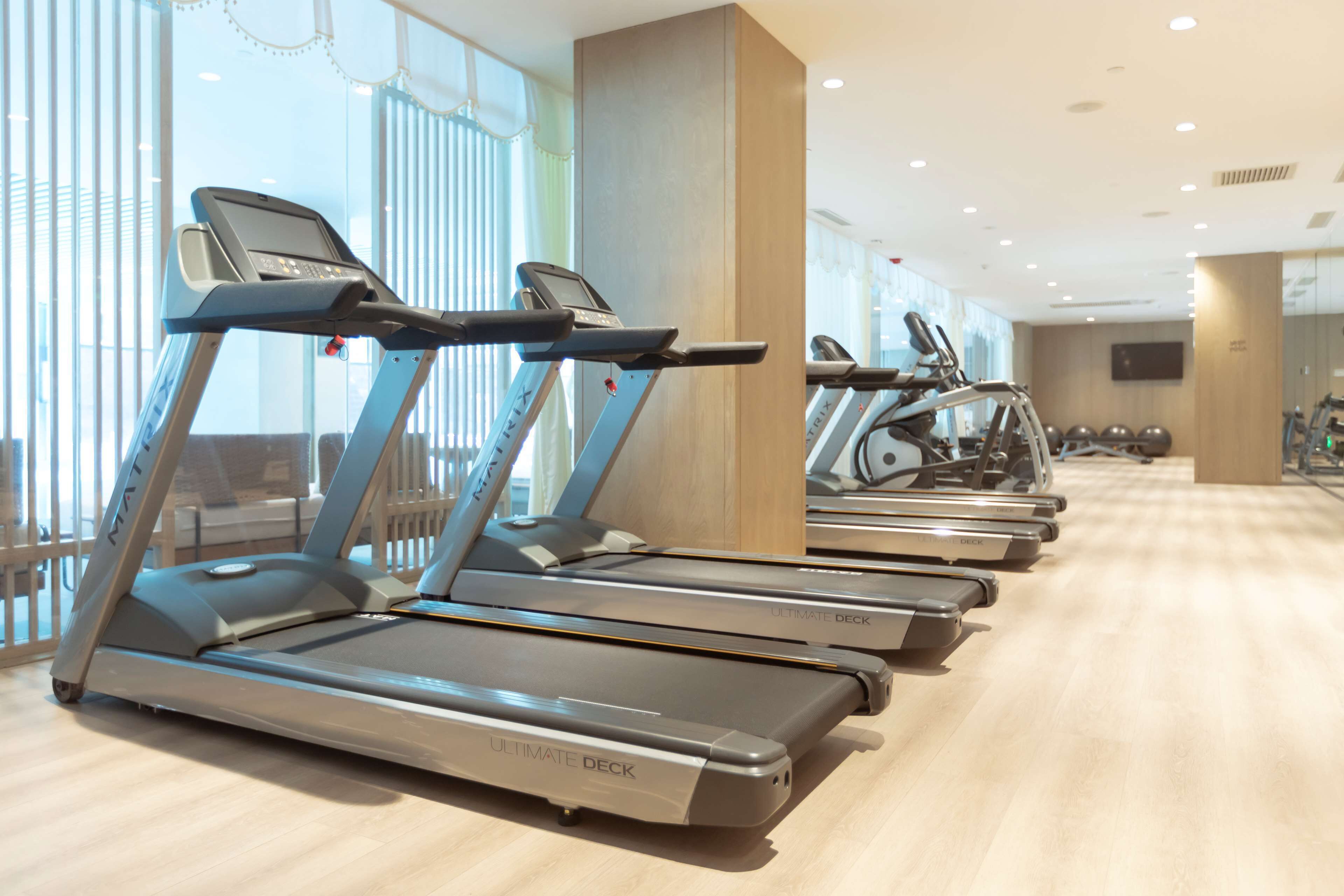 Varias cintas de correr en un gimnasio con amplios ventanales y suelo de madera.