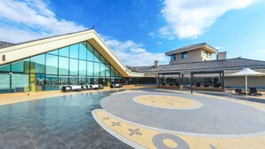 A spacious outdoor area with a modern building featuring large glass windows and a curved seating area. - Hilton Lijiang (Lijiang)