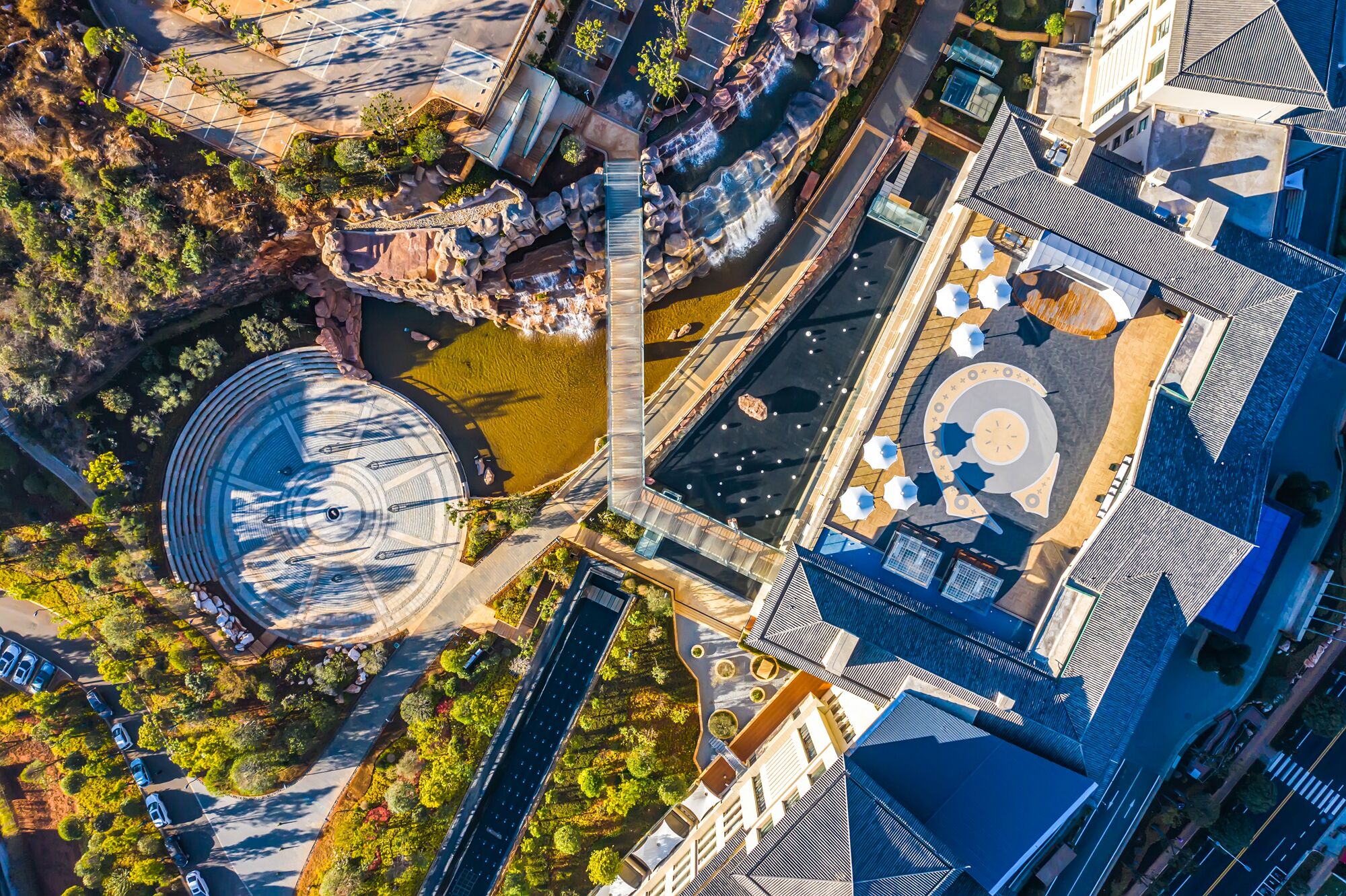 An aerial view of a modern building with a circular plaza, a water feature, and a parking area.