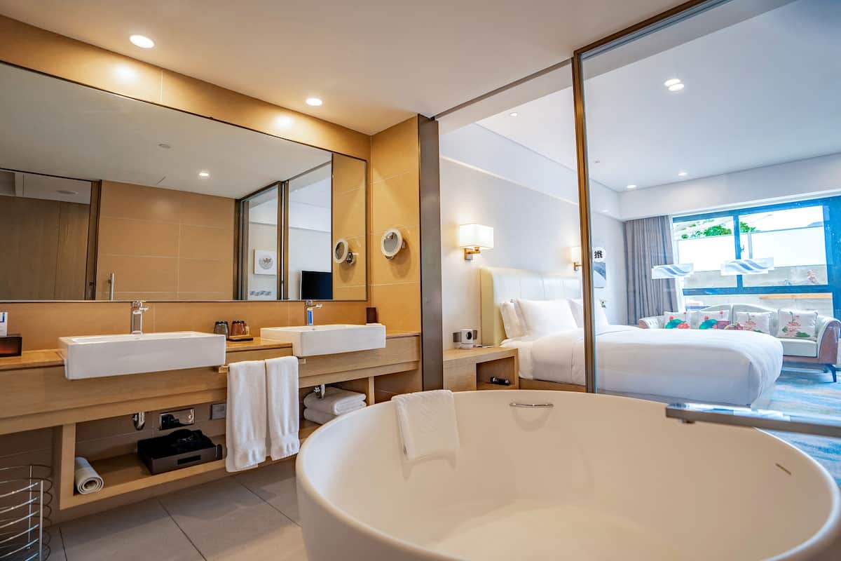 A modern hotel bathroom with a large bathtub, two sinks, and a large mirror.