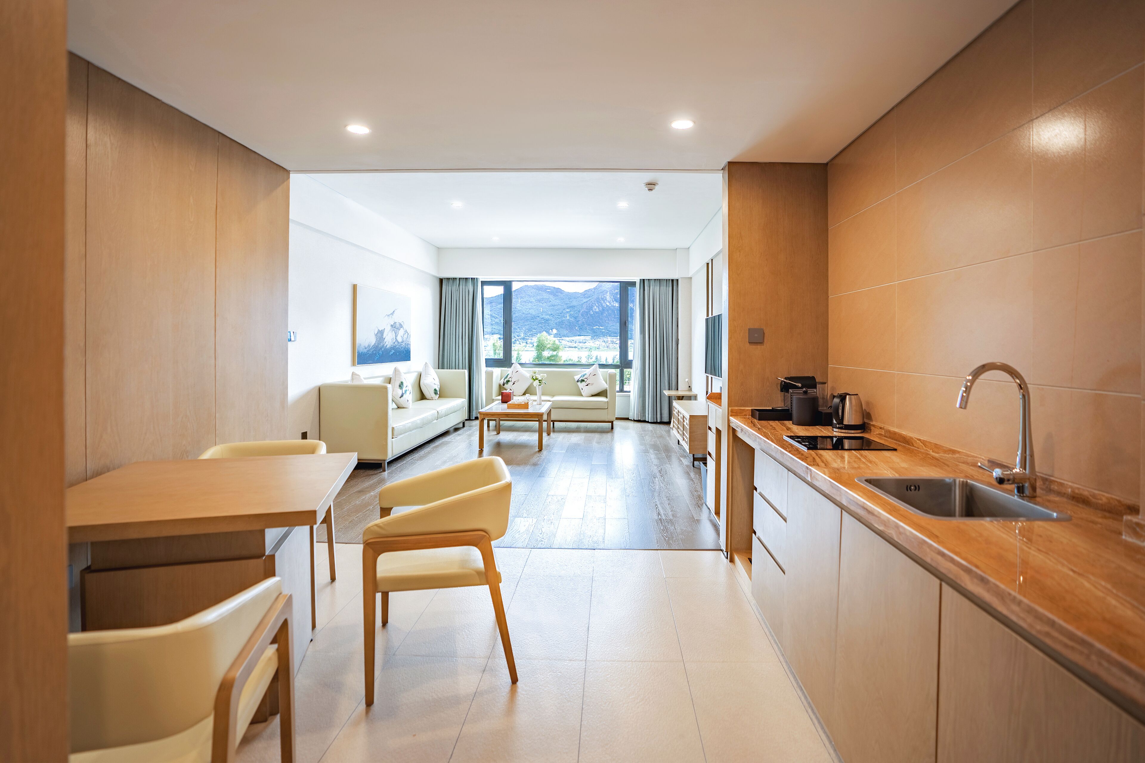 A modern kitchen with a dining area, a sofa, and a view of the mountains.