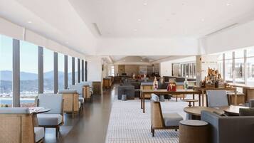 A spacious hotel lobby with high ceilings, large windows offering a view of the mountains, and a variety of seating arrangements including sofas, chairs, and tables.