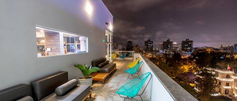 Terraza en la azotea con asientos y vista nocturna de la ciudad.