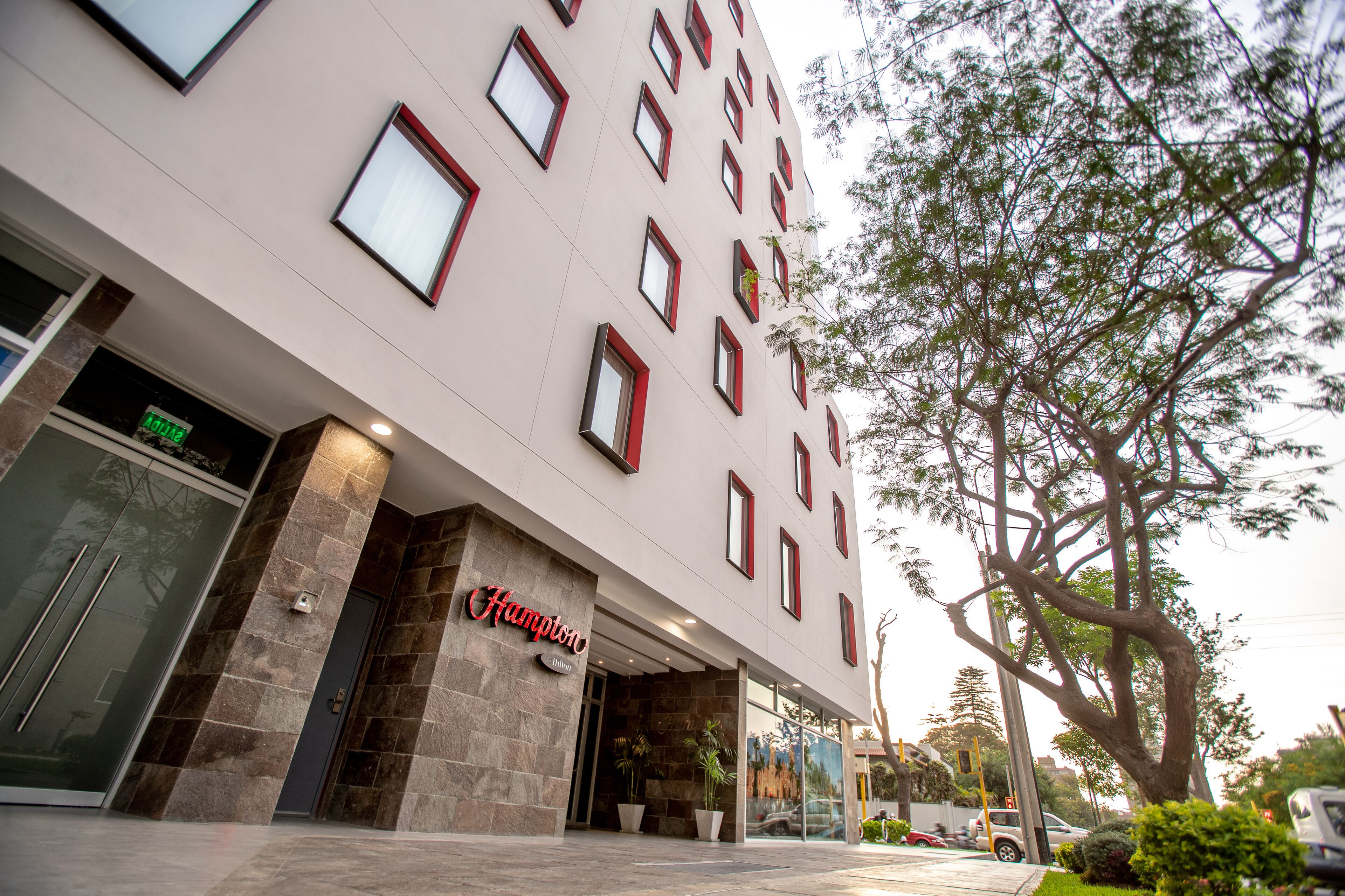 Un hotel moderno con fachada de piedra, múltiples ventanas y una entrada destacada.