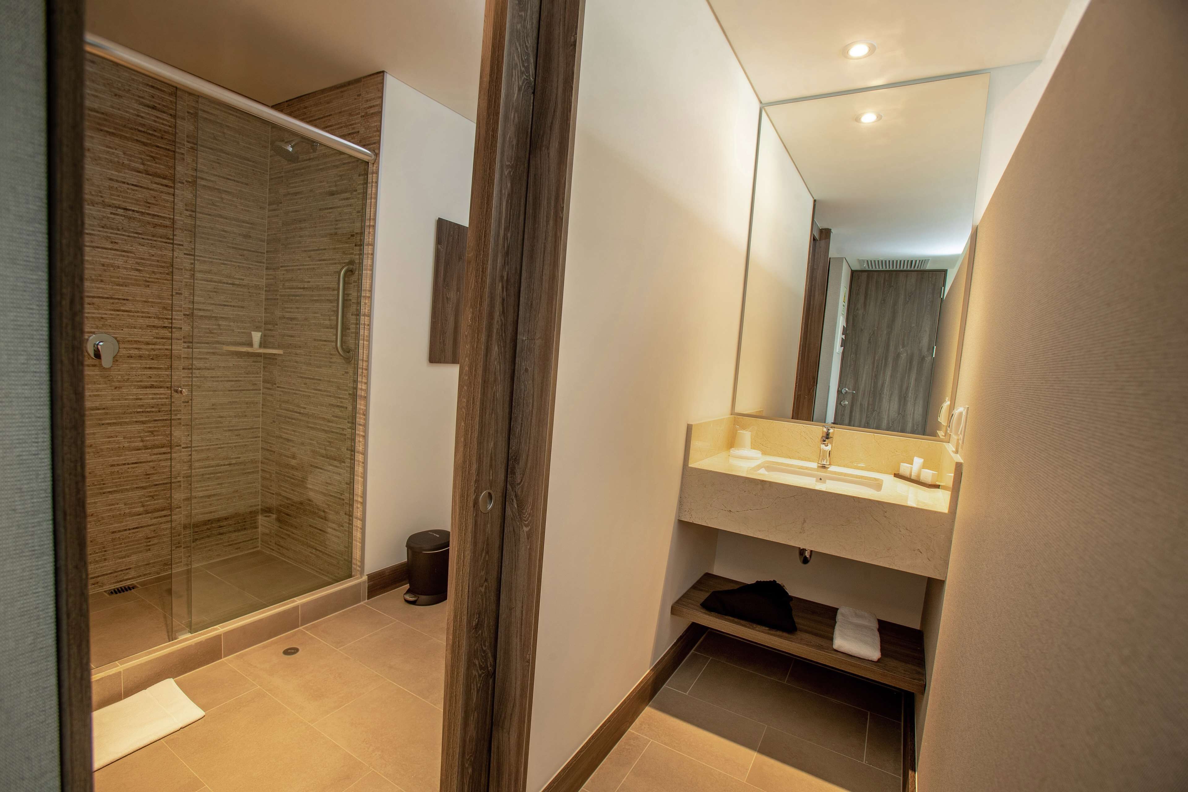 Een moderne badkamer met een douchecabine van glas, een houten wastafelmeubel en een grote spiegel.