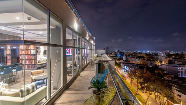 A modern library with glass walls, seating areas, and a view of the city at night. - Hampton by Hilton Lima San Isidro (Lima)