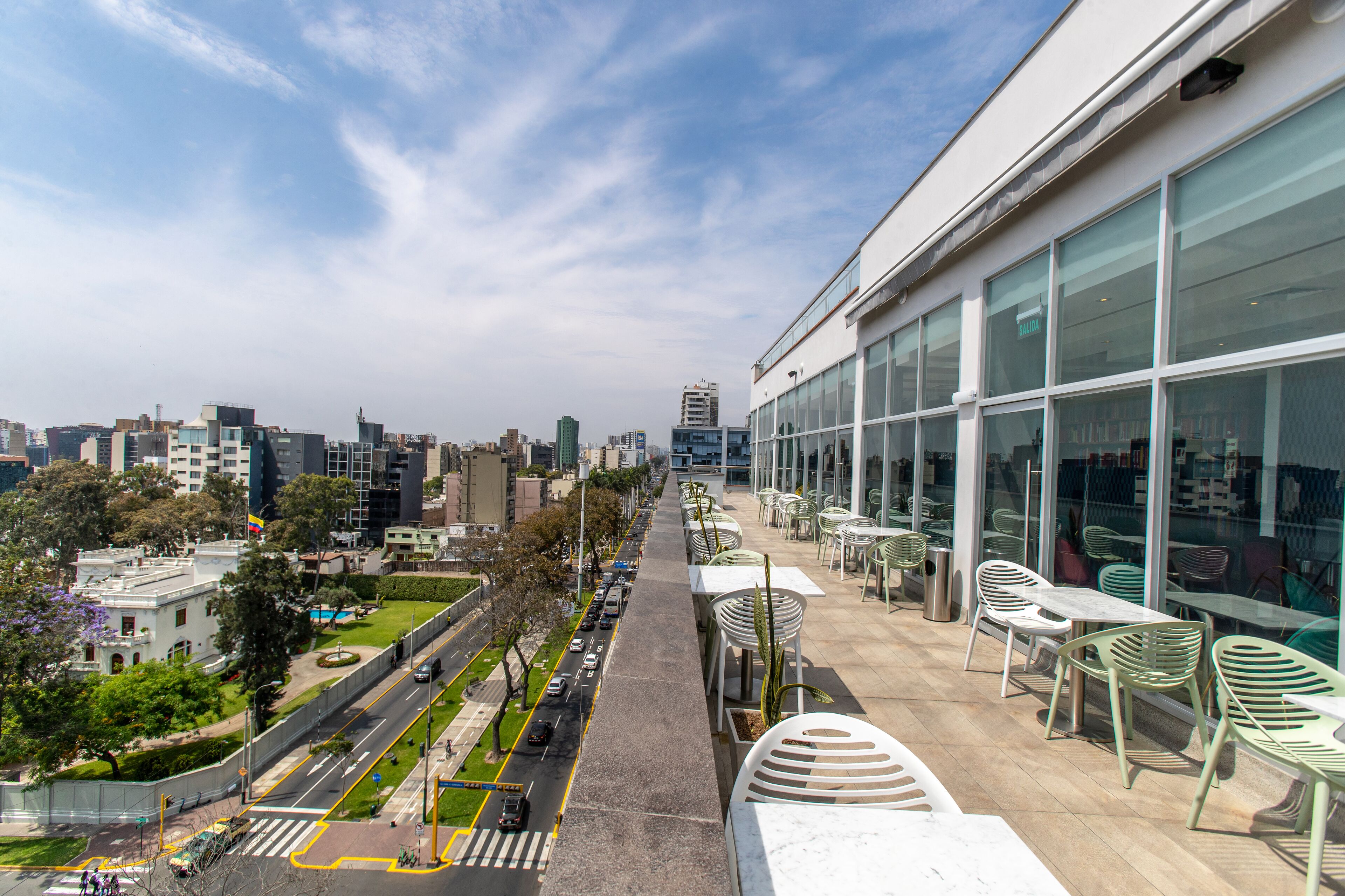 Vista urbana desde un balcón, con calle, árboles y edificios modernos.