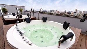 A hot tub with a city view, surrounded by chairs and a wooden deck. - Hampton by Hilton Lima San Isidro (Lima)