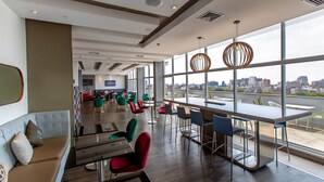 A modern interior with a bar area, seating, and large windows offering a city view. - Hampton by Hilton Lima San Isidro (Lima)