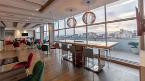 A modern restaurant with large windows, wooden flooring, and a view of the city skyline. - Hampton by Hilton Lima San Isidro (Lima)