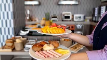 A buffet setup with various food items including fruits, pastries, and meats.