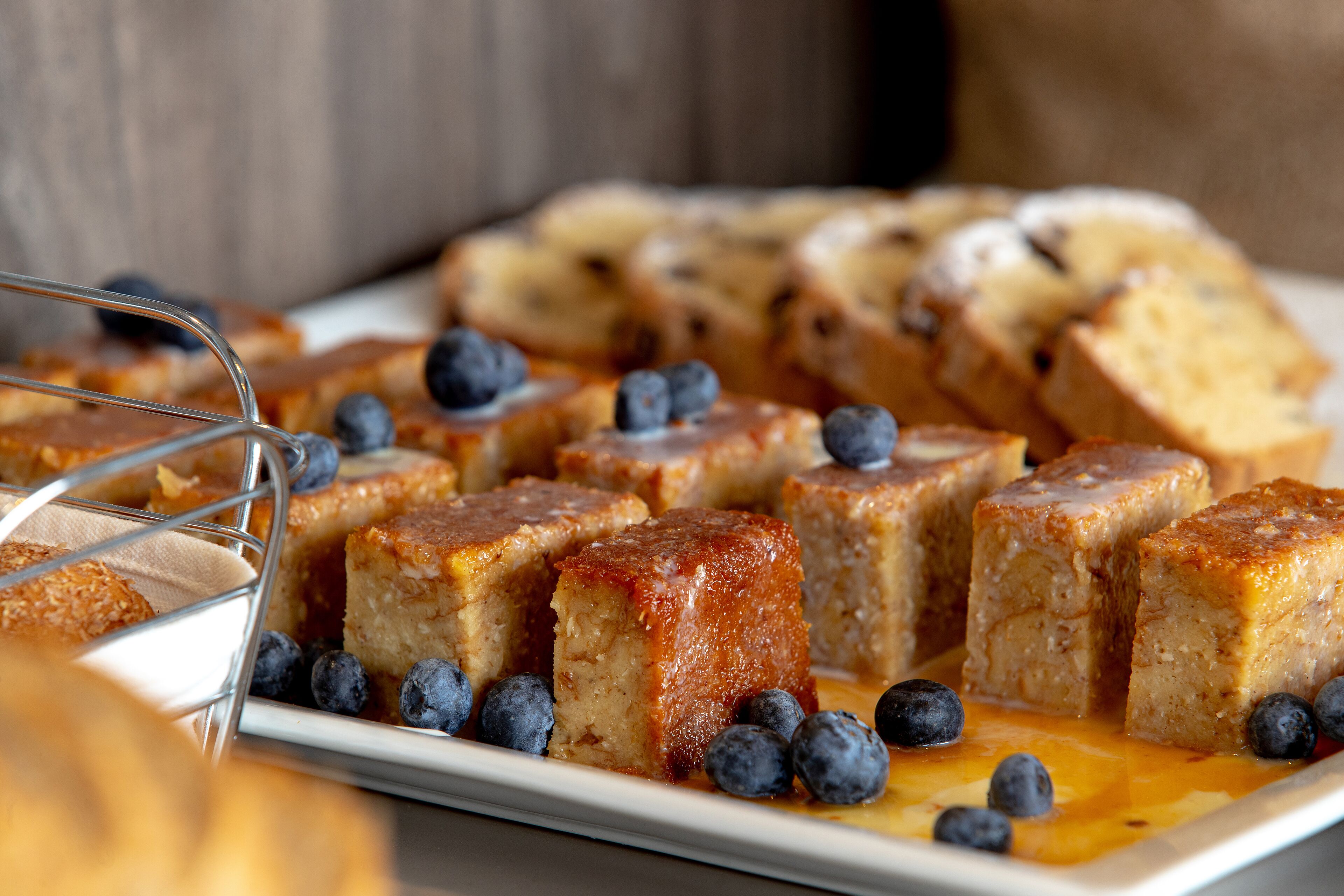 A tray of square-shaped, caramel-topped desserts with blueberries on a white plate.