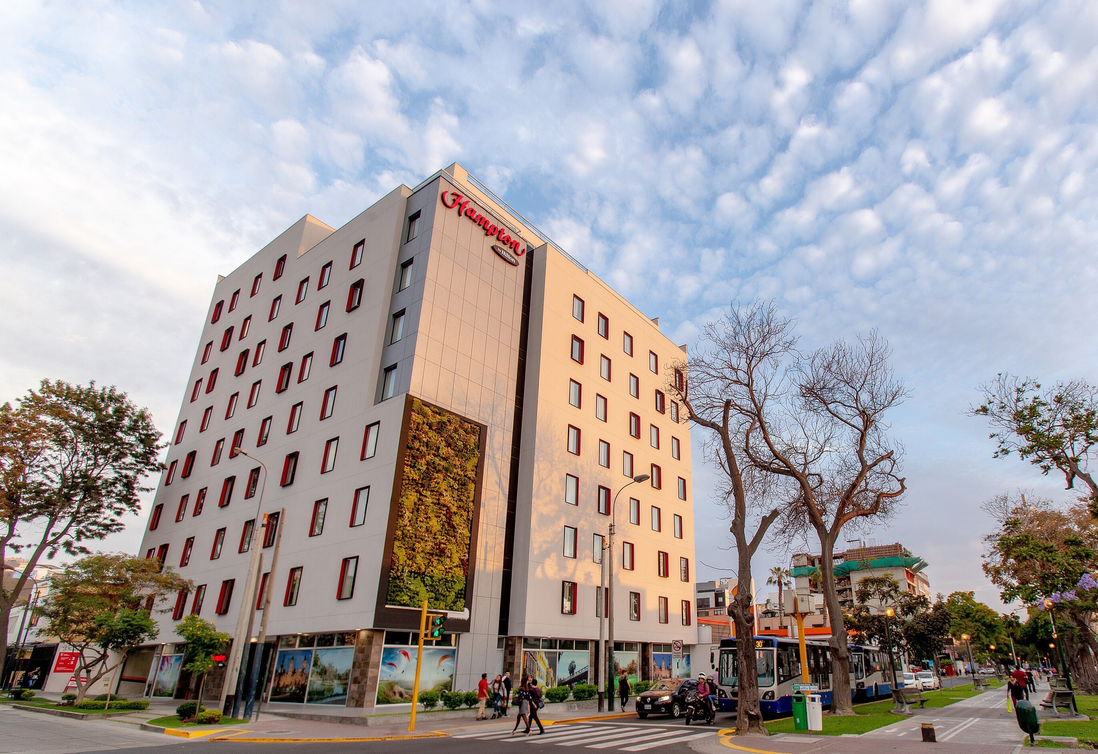 A modern hotel with a prominent 'Hampton' sign, multiple floors, and a large vertical garden feature.