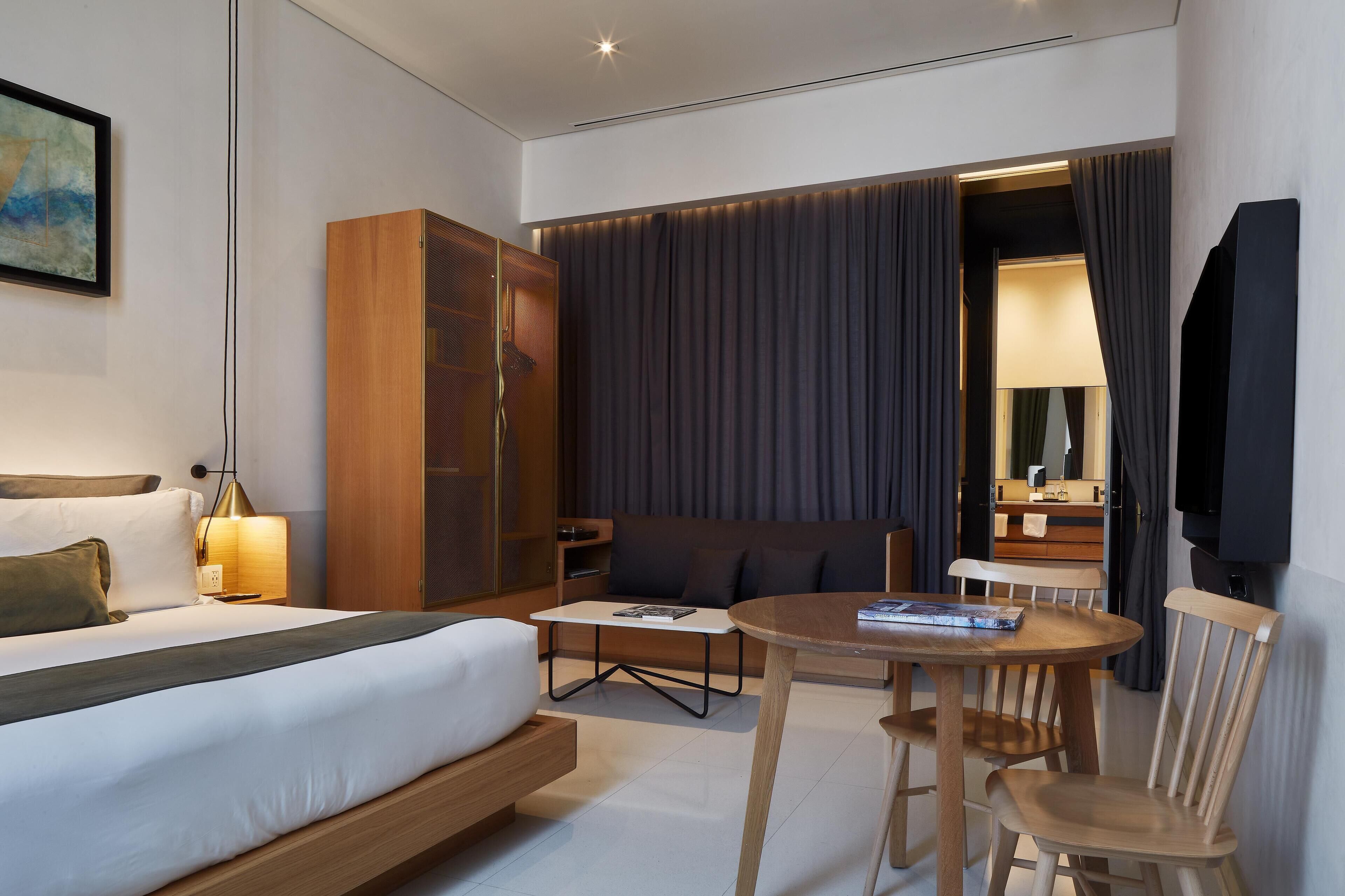 Una habitación de hotel moderna con cama, escritorio, silla, armario y un espejo grande.
