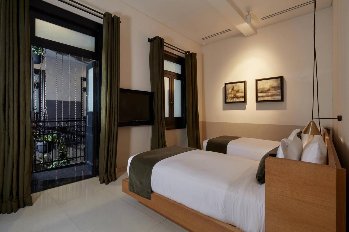 A hotel room with two beds, a TV, artwork, and a balcony with curtains.