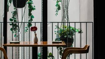 A room with a wooden table, two chairs, a vase with a red flower, and hanging plants.