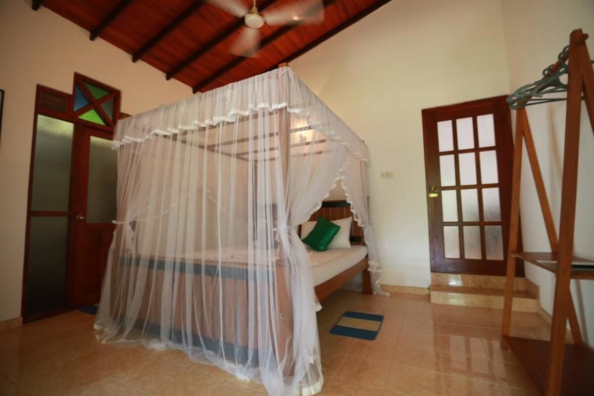 Una habitació amb un llit sota una estructura de cortina, una porta de fusta i una escala.