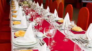 A long dining table with red chairs, set with white napkins, plates, and wine glasses. - Hotel Restaurante América (A Estrada)