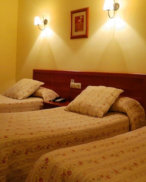A hotel room with two beds, each with floral-patterned bedding and matching pillows. There are wall-mounted lamps on either side of a framed picture above the beds. - Hotel Restaurante América (A Estrada)