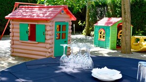 A picnic setup with a table covered by a blue tablecloth, surrounded by two small wooden playhouses with red roofs. - Hotel Restaurante América (A Estrada)