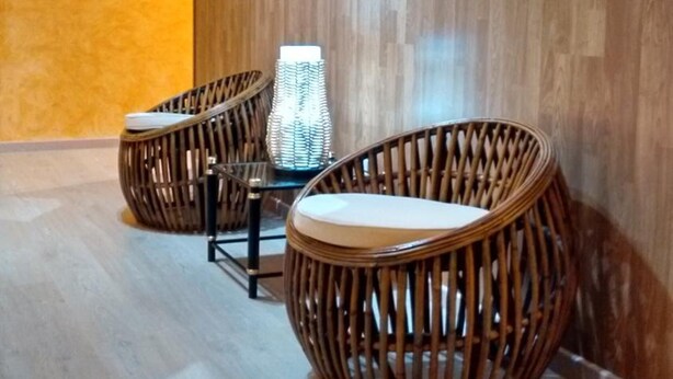 A room with a wooden floor, a wall with a wavy pattern, and two wicker chairs with cushions. - Hotel Restaurante América (A Estrada)