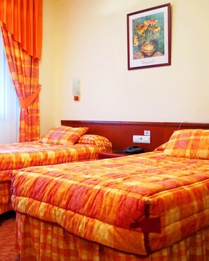 A hotel room with two beds, orange checkered bedding, a painting of flowers, and a telephone on the nightstand. - Hotel Restaurante América (A Estrada)