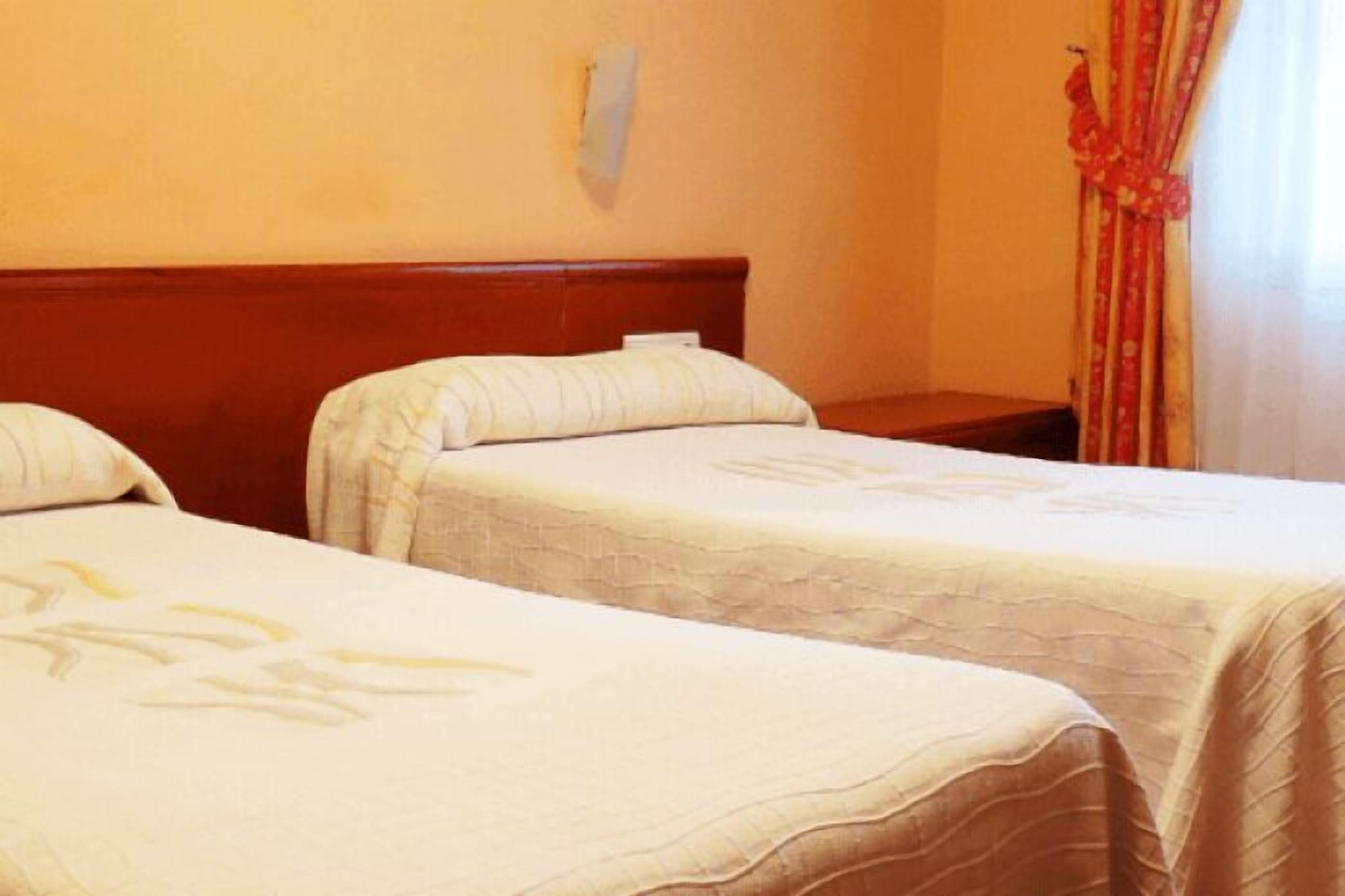 A hotel room with two single beds, a wooden headboard, a small bedside table, and a red curtain.