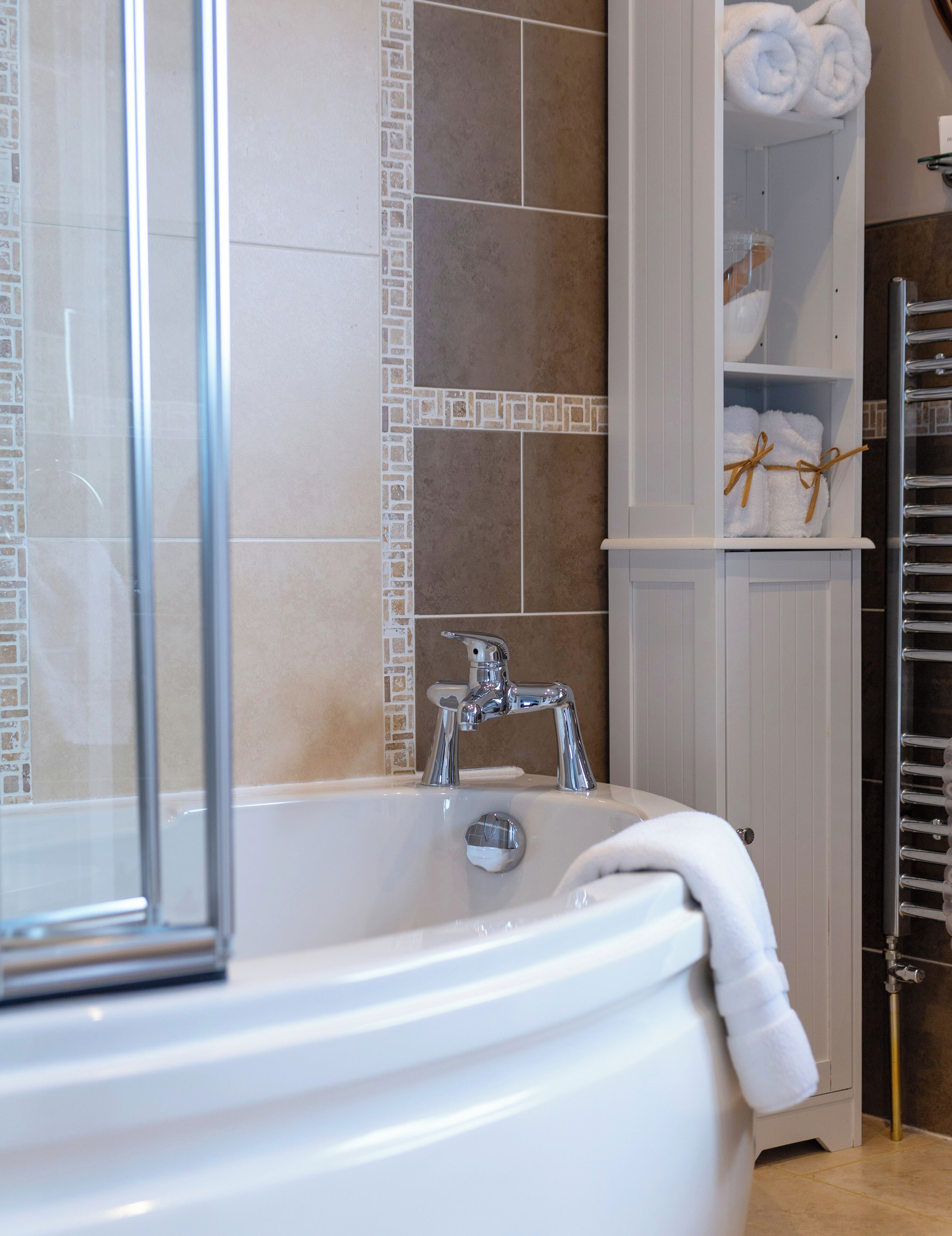 A bathroom with a bathtub, a glass shower enclosure, and a towel rack.