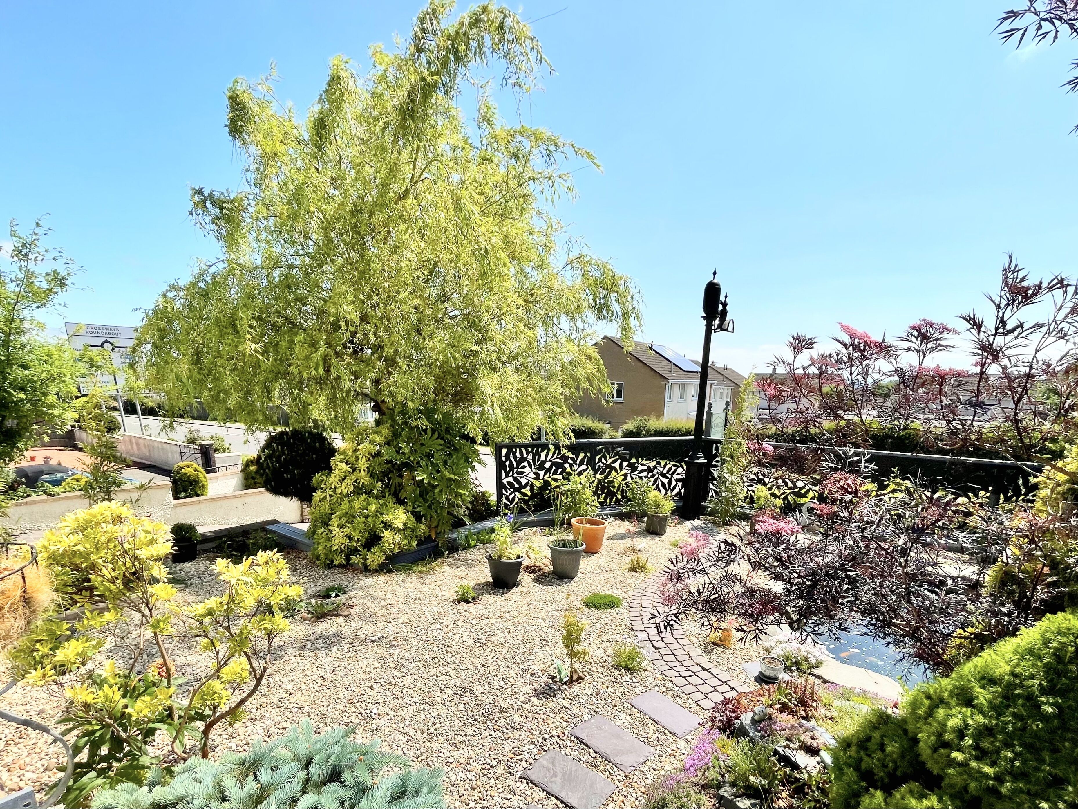 Un jardin avec différentes plantes, un sentier et une maison en arrière-plan.